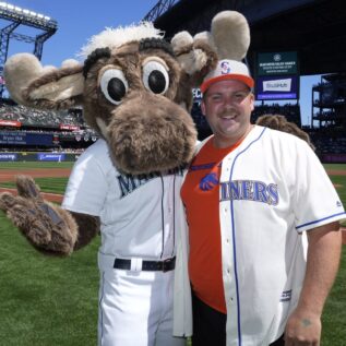 A person poses on a baseball field with the Seattle Mariners mascot