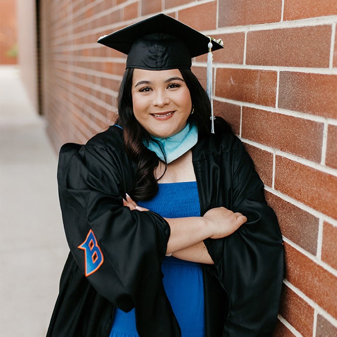 Headshot of Maria Garcia De la Cruz in her Boise State regalia, leaning on a brick wall.