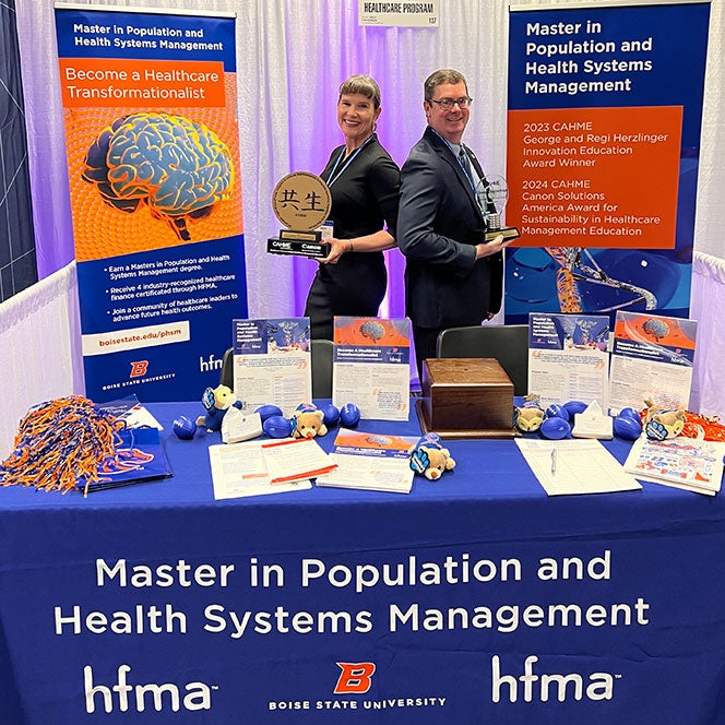 Jenni Gudapati and Todd Nelson stand back-to-back holding the program's awards at the program's exhibit booth at the congress.