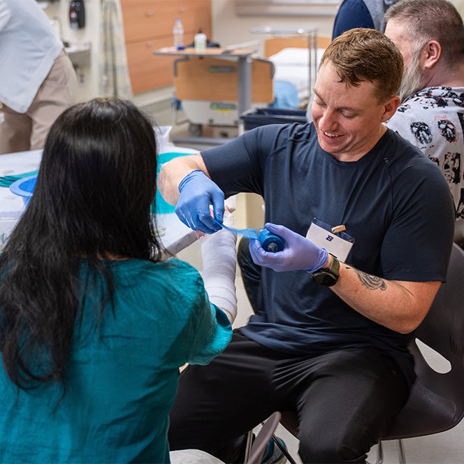 A nurse practitioner student wraps blue tape around a cast.
