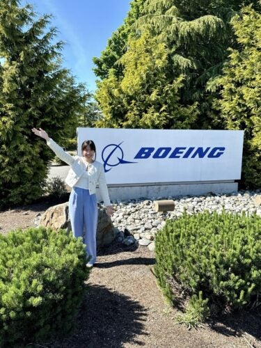 CTMBA student Christine Nguyen stands in front of a Boeing sign with her arms outstretched.
