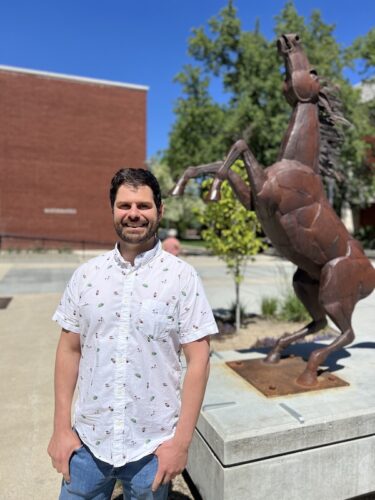 man stands on Boise State campus by Bronco statue