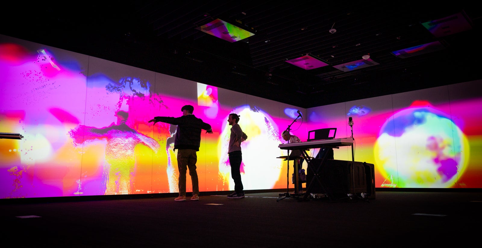 Persons stand in front of art work on a digital screen