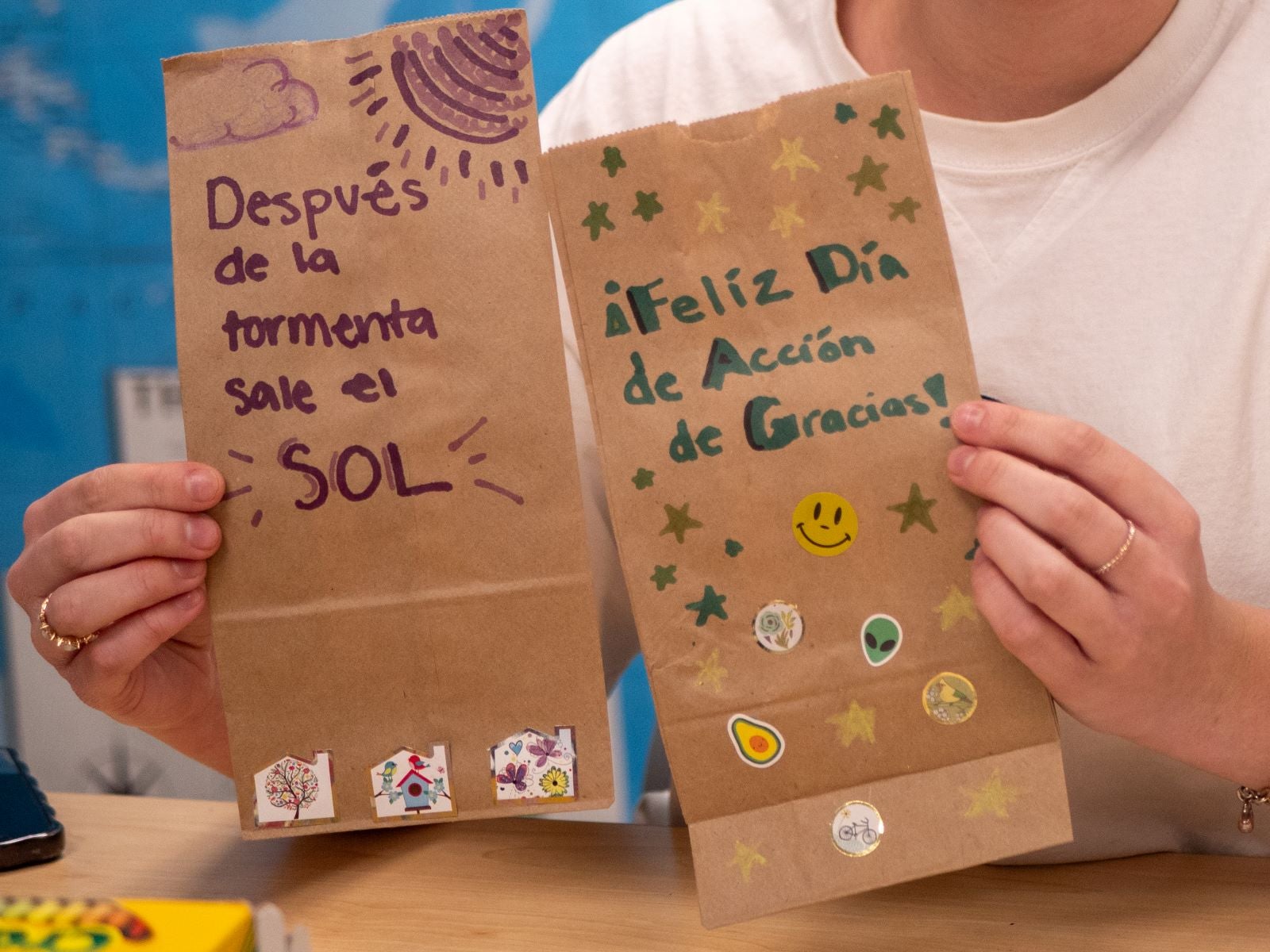 A person holds tow paper bags decorated with sayings in Spanish: After the storm, the sun comes out and Happy Thanksgiving Day