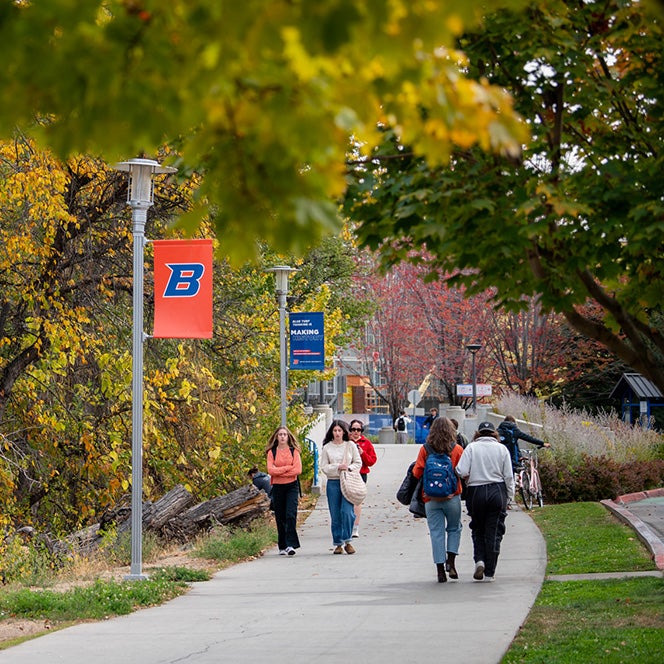 Students walking along the Greenbelt adjacent to campus with Boise State banners hanging on the light poles