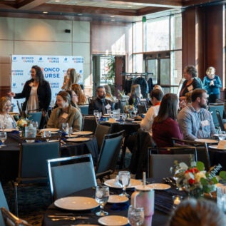 Guests stand and mingle at tables set for dinner in a ballroom.