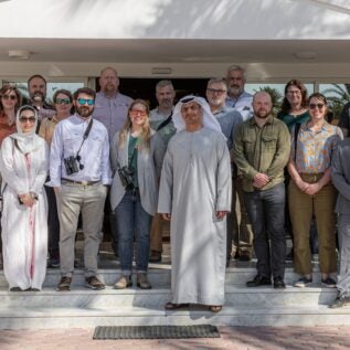 A group of scientists pose in front of a building.
