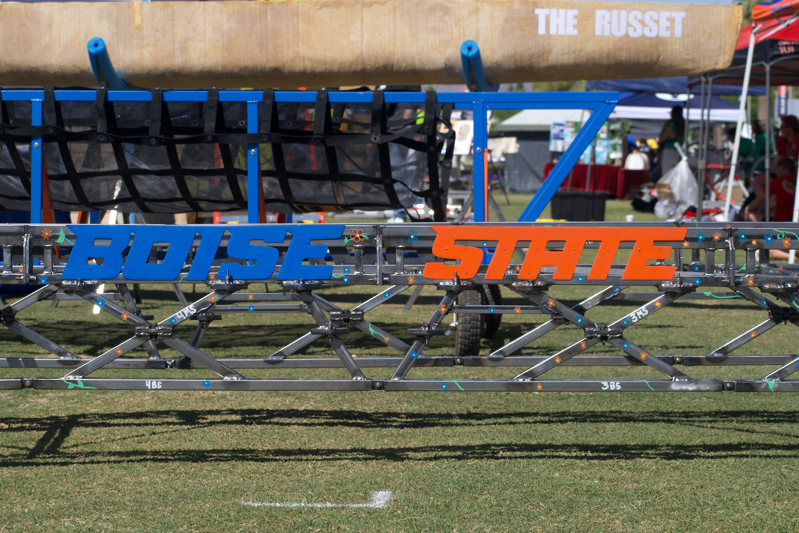 a steel bridge rests on ground with 'Boise State' logo written in blue and orange on its span