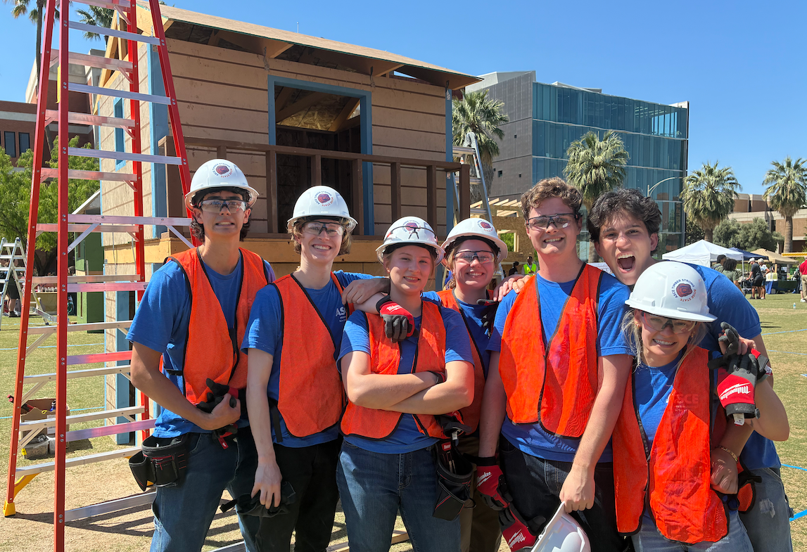 A group of students in hard hats and safety vests pose