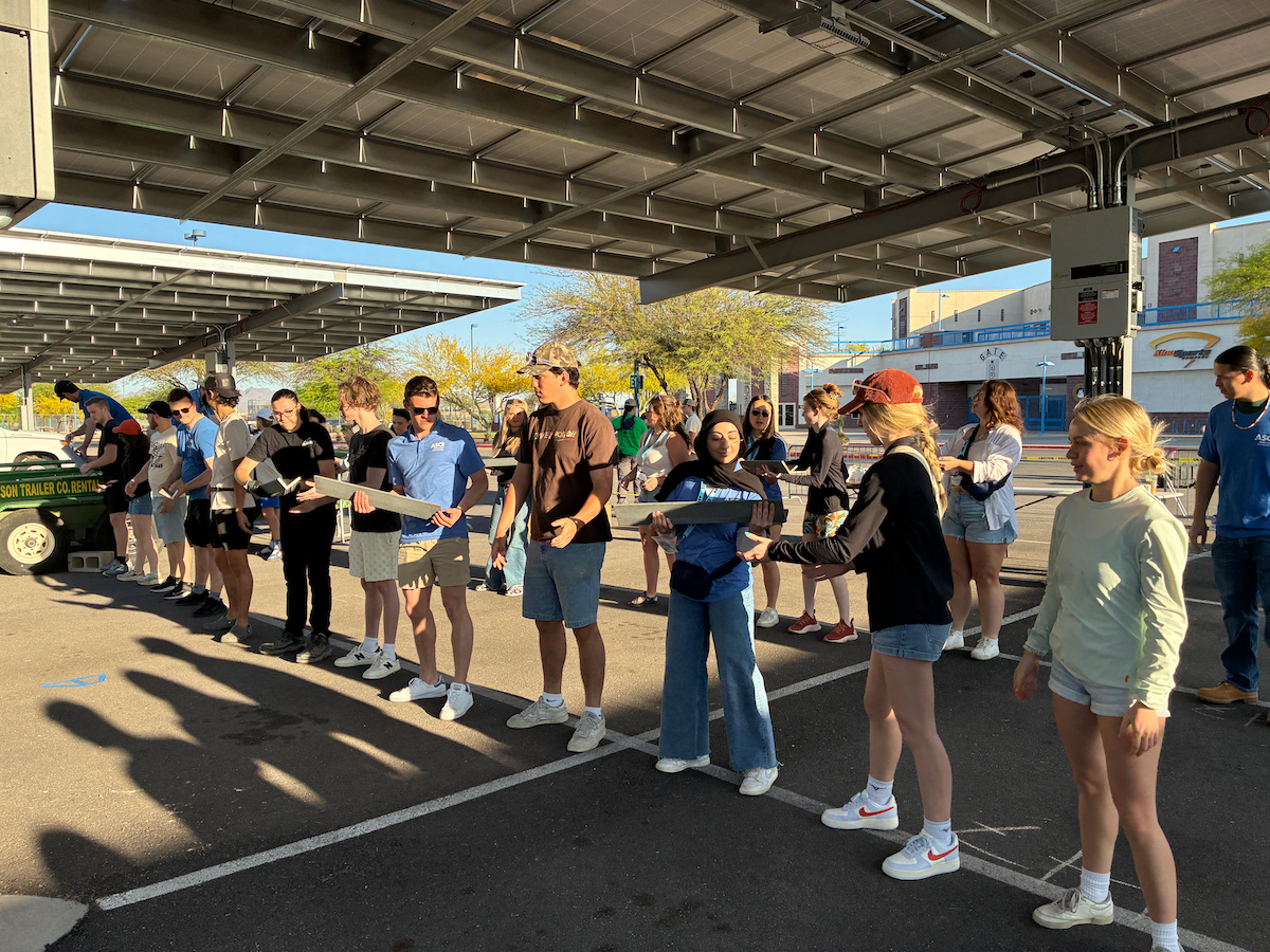 13 students form a line to pass along pieces of steel needed to build bridge.