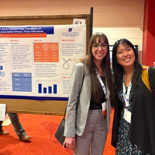 A student and professor stand by a research poster and smile.