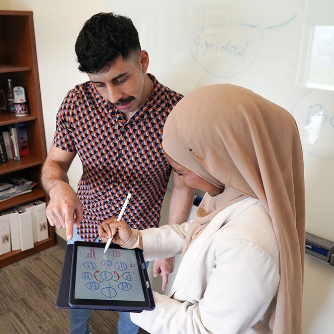male social work student has conversation with female social work student holding a tablet and pencil