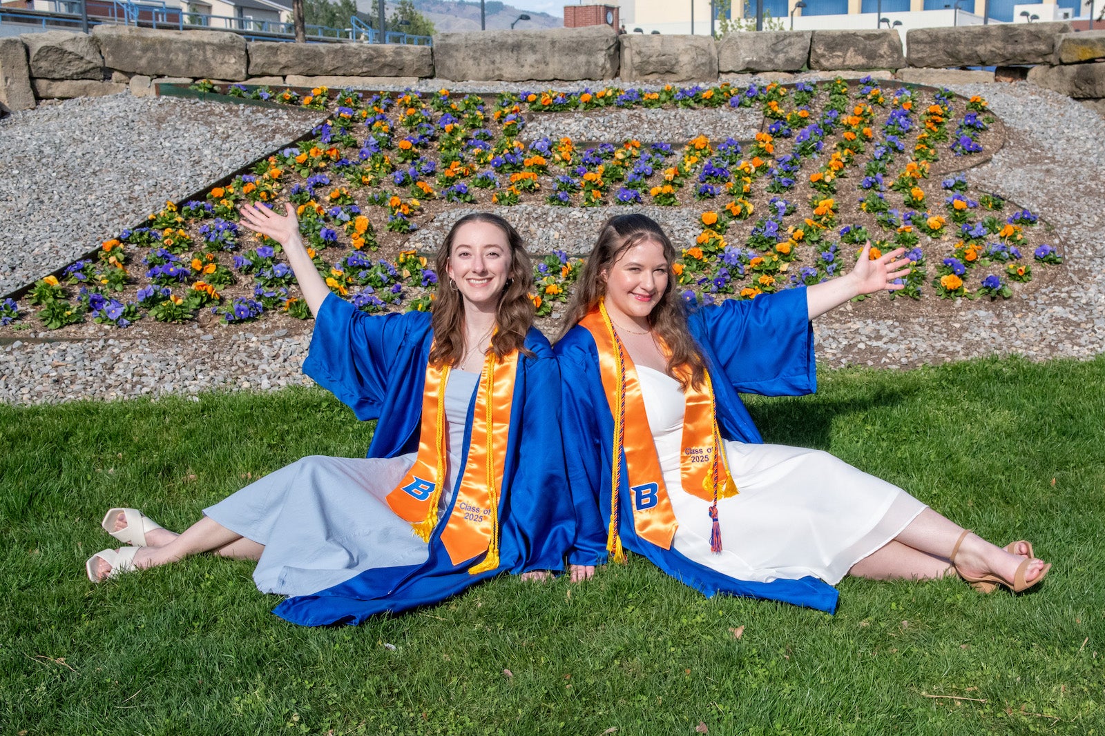 Two persons in regalia pose in front of a flower bed shaped like a letter B