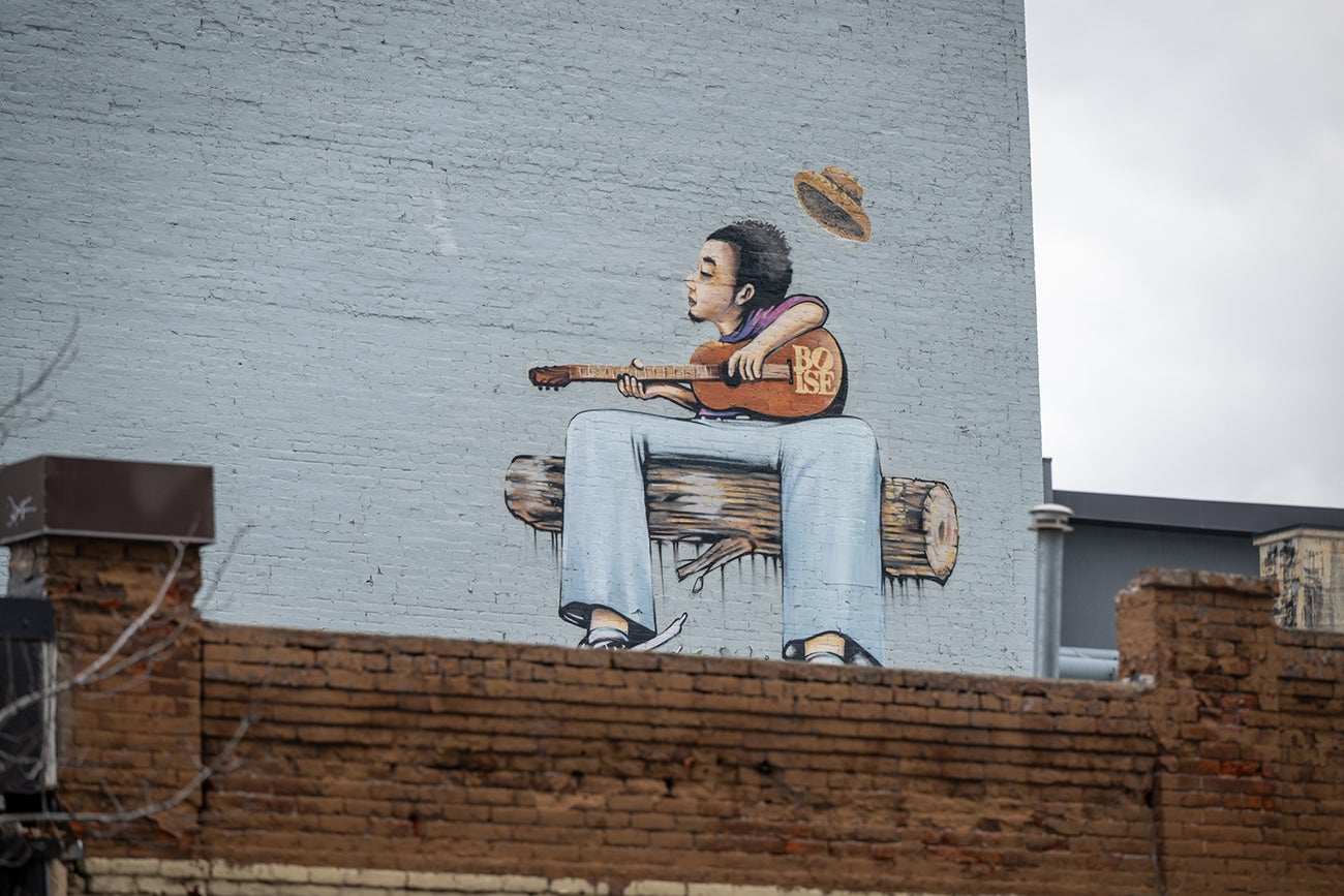 Photo of wall mural, "Groovin," man sitting on log playing guitar.