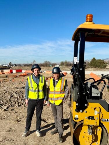 Two persons in protective gear next to heavy construction equipment
