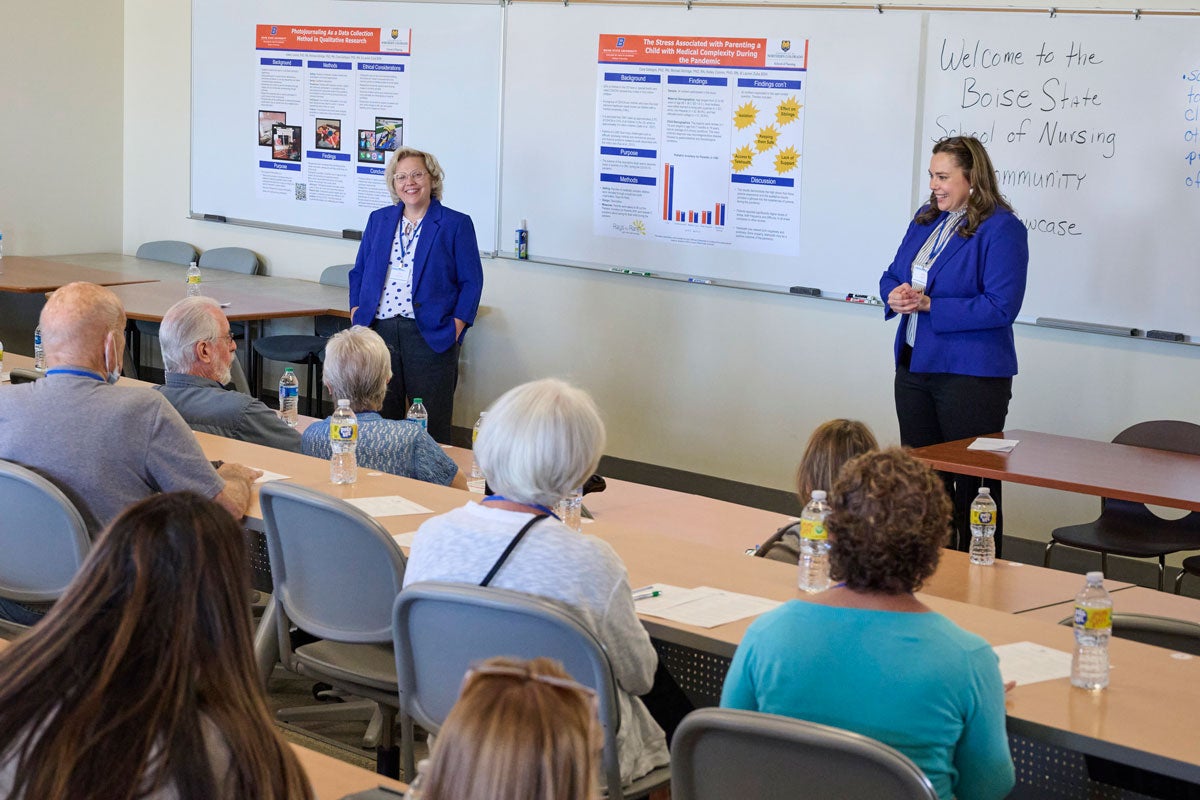 Amy Spurlock and Shelle Poole stand at the front of a lecture hall and talk to people sitting at the tables.