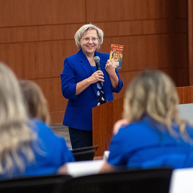 Amy Spurlock holds a book up in front of a room of students and speaks into a microphone.