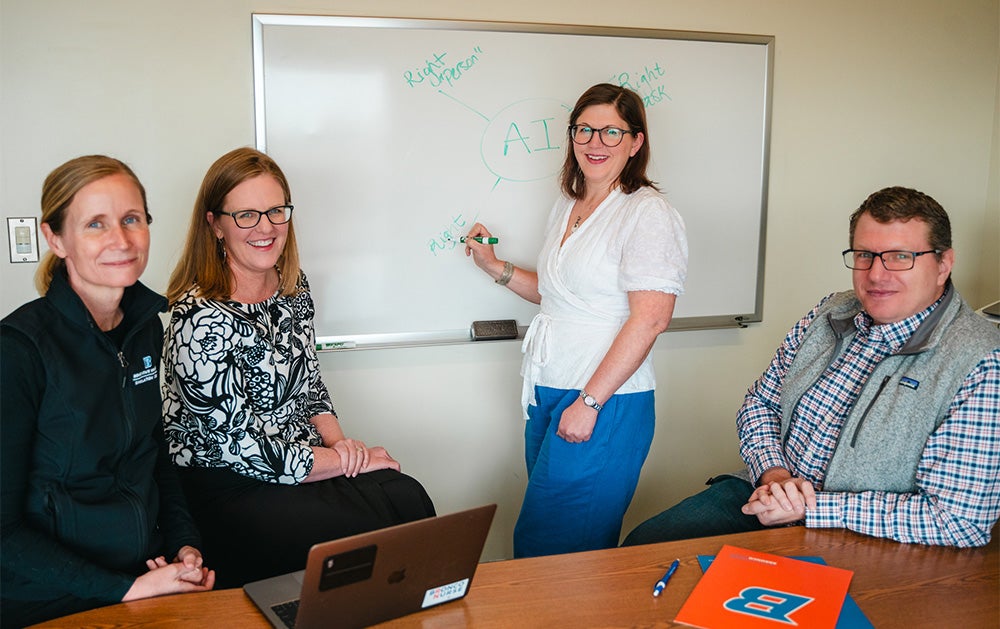 Group photo in a conference room around a table with a white board on the wall.
