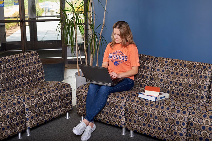 Woman sits on couch looking at laptop