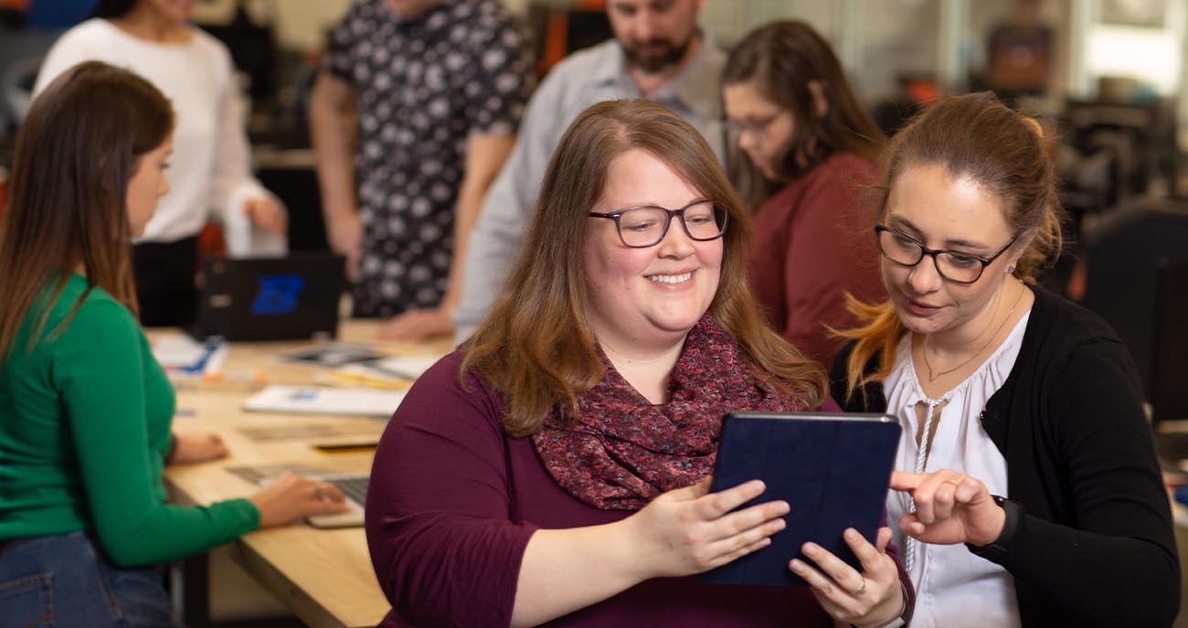Two integrated strategic communication students stand looking at an iPad.