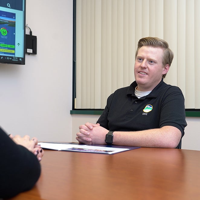 A Boise State student talks with another student while sitting at a table.