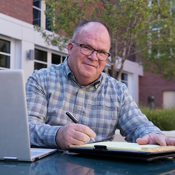 Online MBA student sits with notebook and laptop.