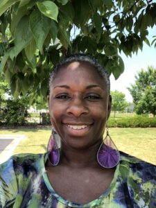 Pia Valere Adams stands under a tree and smiles.