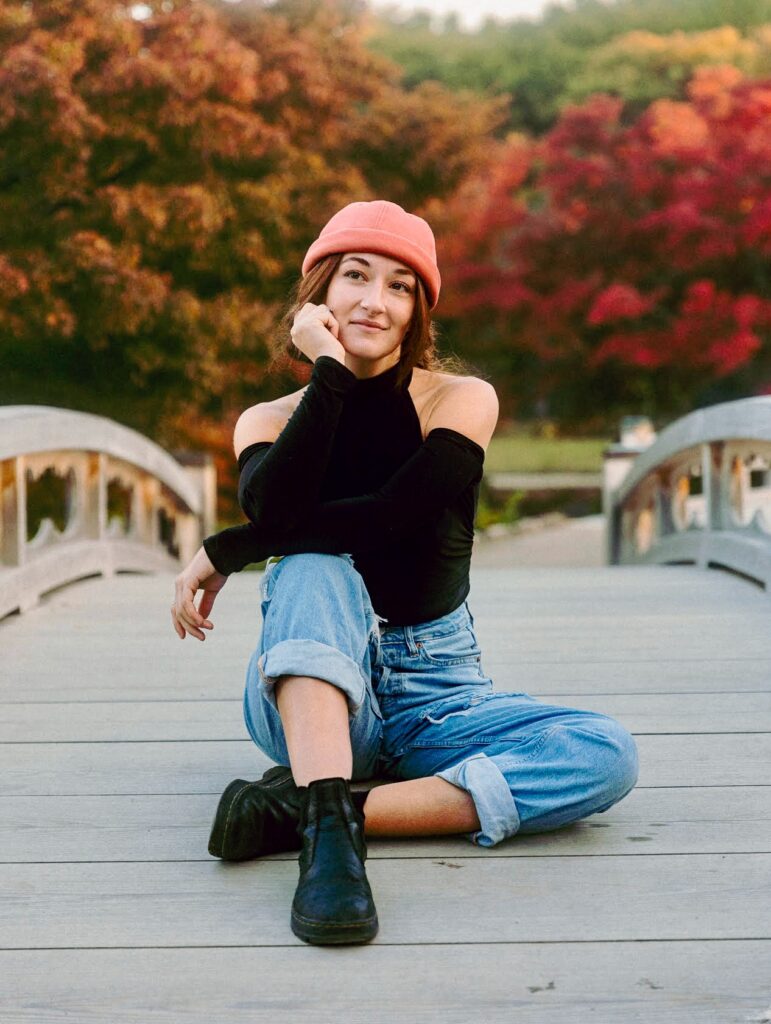 Photo of Abigail Wisdom, sitting on a bridge with trees in the background.