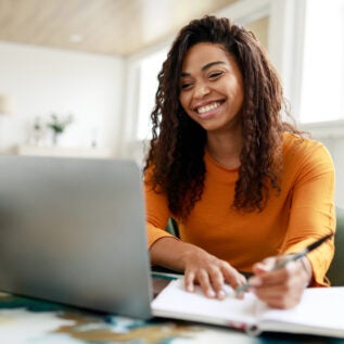 A woman sitting at a desk taking notes in front of a laptop