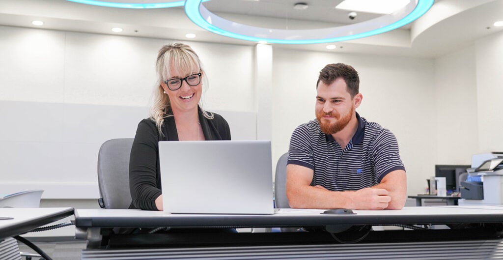 Cybersecurity student, Kris Pruett, working on a computer with a coworker