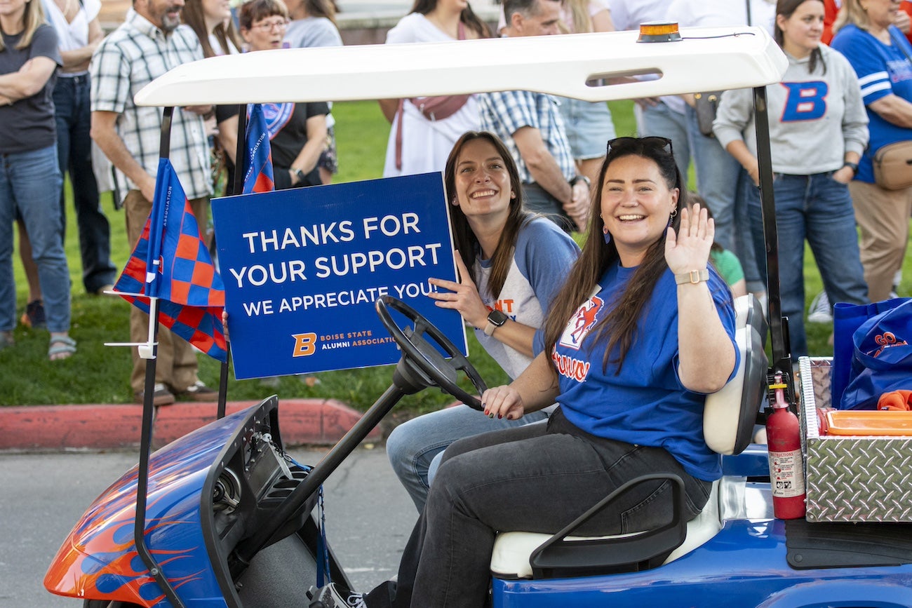 Boise State homecoming Parade: Two persons wave from a golf cart.