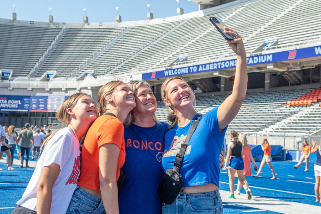 Four people stand together to take a group selfie on the blue turf