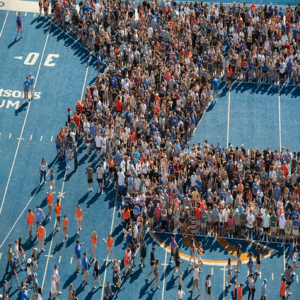 Students, families, and faculty form b on blue turf