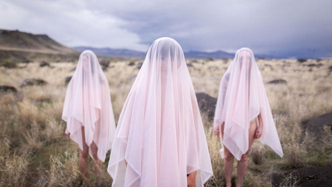Three veiled women stand in a desolate, rocky landscape
