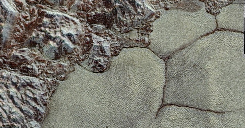Reddish-brown rough terrain transitioning to beige cracked polygons, resembling geological surface features.