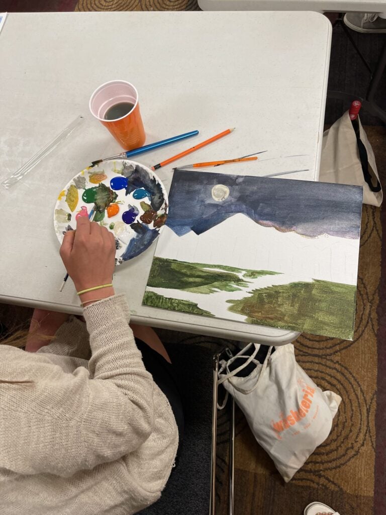 An artist paints a mountain landscape scene.