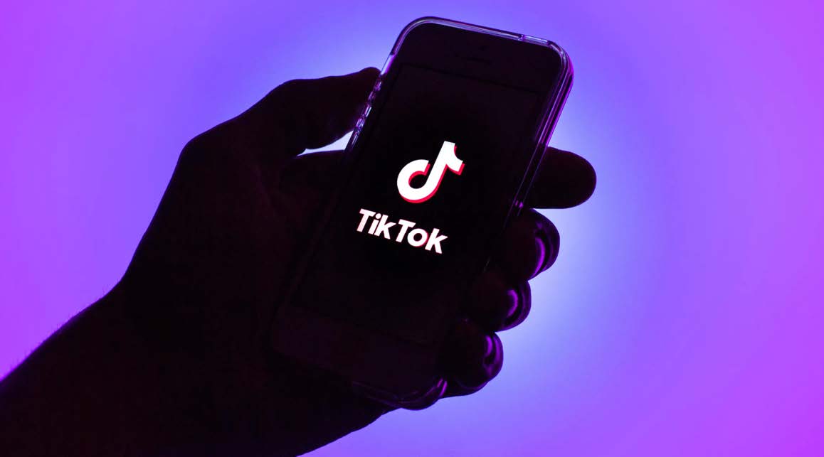 A sillohuette of a hand holding a phone with the TikTok logo on screen