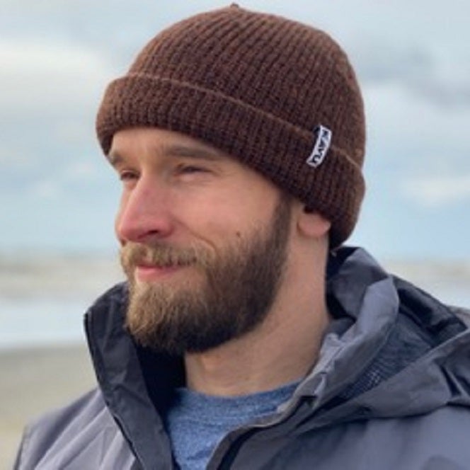 Mark at an Oregon beach on a cloudy Oregon day wearing a gray rain jacket and a brown cap