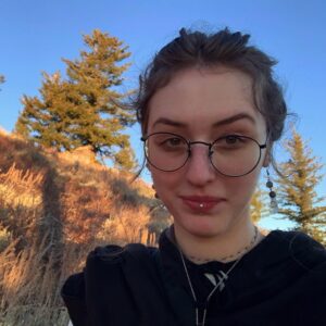 A headshot of Keira smiling at the camera surrounded by an outdoor landscape at sunset