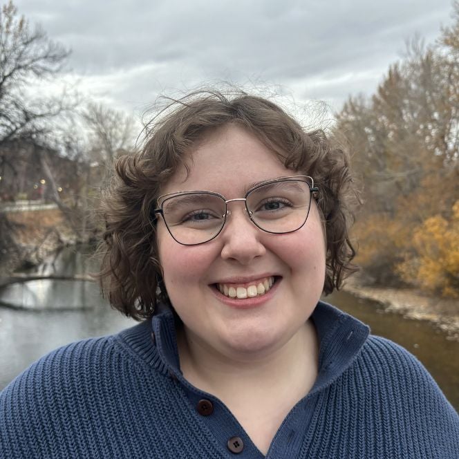 Photograph of Amelia Jobe (curly brown hair, glasses, pale with freckles) in a blue sweater on Friendship Bridge