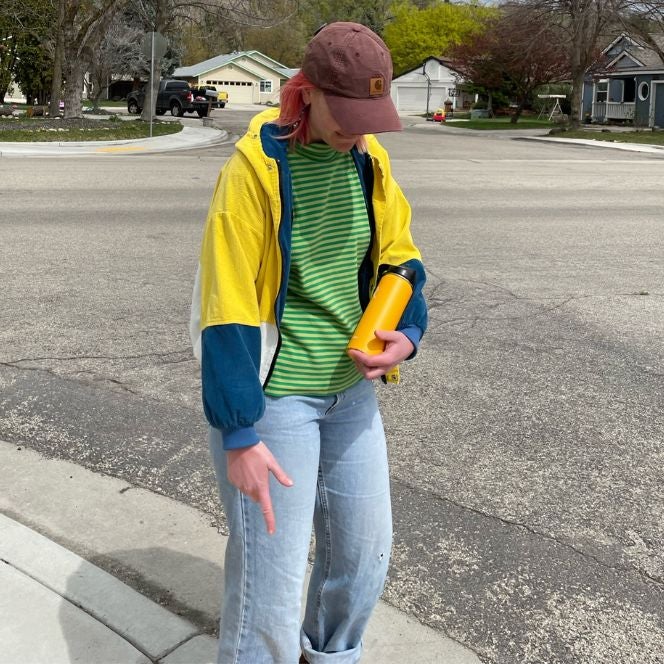Naomi walking on the sidewalk, head tilted down so you can only really see their brown hat and part of their pink hair.