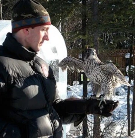 Travis Booms holding a raptor in the field