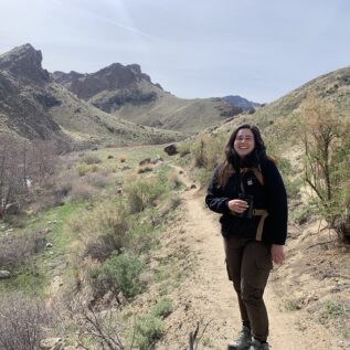 Raptor Biology student Ashley Santiago standing with a backpack in the MNSRBOP National Conservation Area