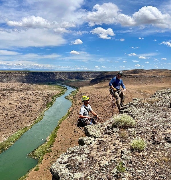 Two people climbing up over the lip of a canyon wall in the NCA