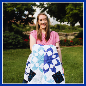 Cassie stands holding her fireworks quilt, featured in Quiltfolk, Issue 20. The photo was taken by Azuree Wiitala