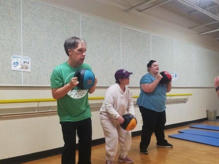 Three people standing in a gym with a ball in hand going through drills.