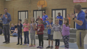 Zach Arlit lined up with seven elementary school kids singing and dancing while using their hands.