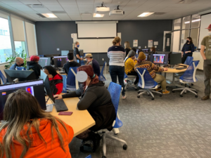 Wide picture frame of the classroom with students sitting at a few tables.