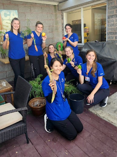 Seven students wearing nursing uniforms holding heart healthy vegetables.
