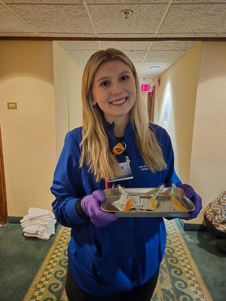Student smiles while holding tray of vaccines.